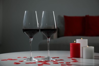 Burning candles, wine in glasses and paper hearts on table indoors