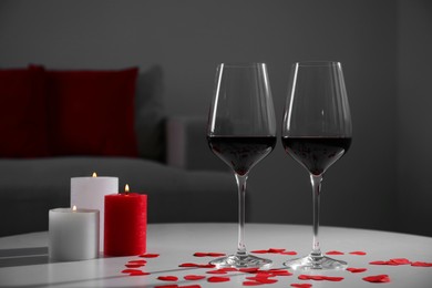 Photo of Burning candles, wine in glasses and paper hearts on table indoors