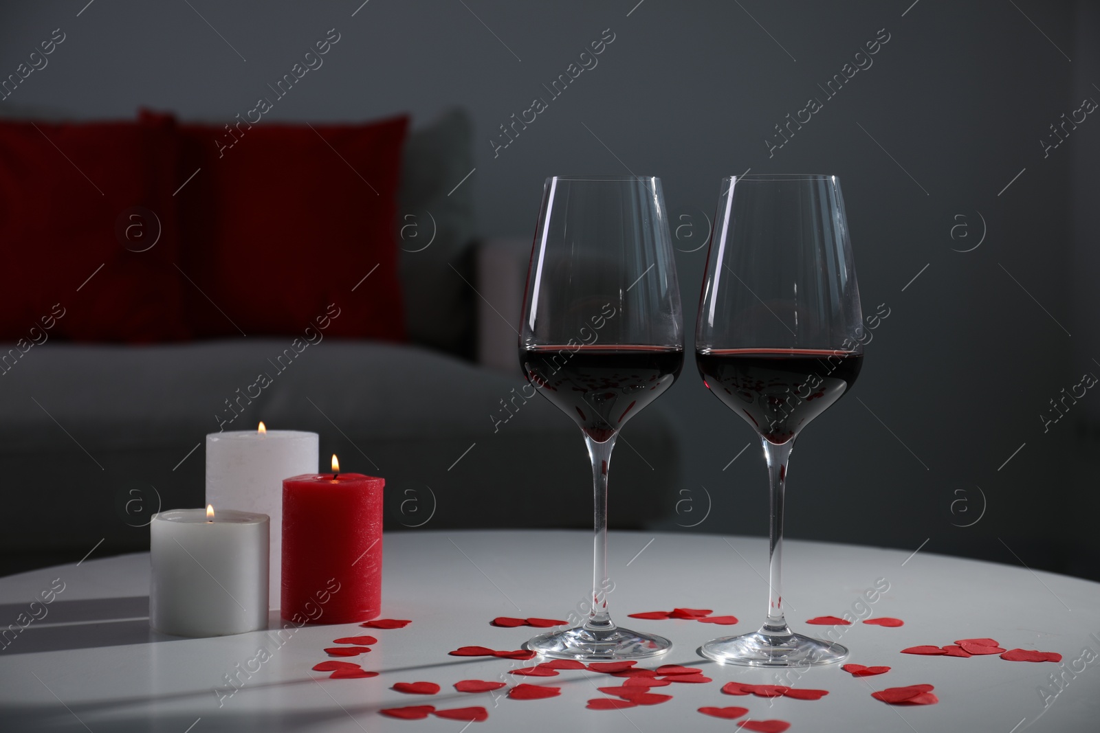 Photo of Burning candles, wine in glasses and paper hearts on table indoors