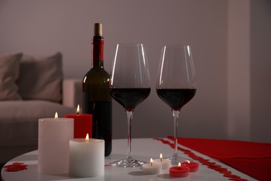 Photo of Burning candles, wine and paper hearts on table indoors