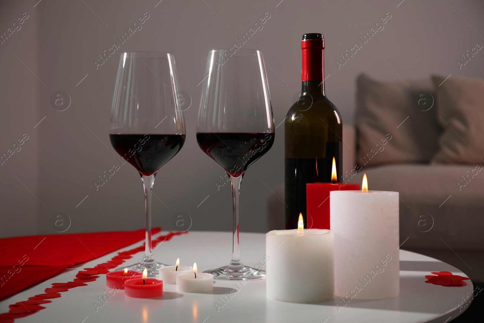 Photo of Burning candles, wine and paper hearts on table indoors