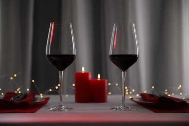 Photo of Burning candles and wine in glasses on table against blurred lights