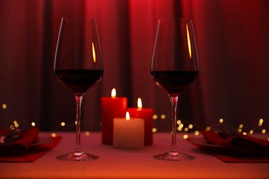 Photo of Burning candles and wine in glasses on table against blurred lights