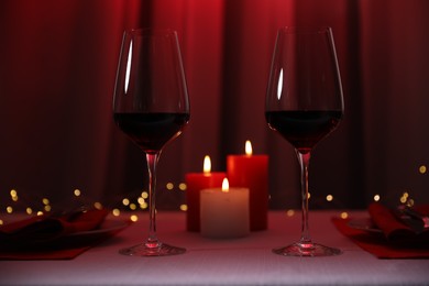 Photo of Burning candles and wine in glasses on table against blurred lights