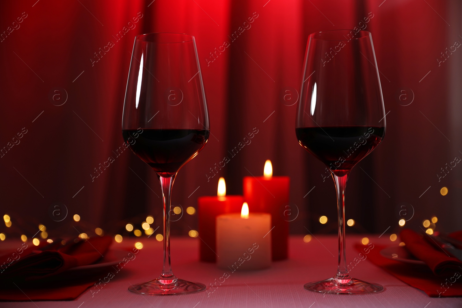 Photo of Burning candles and wine in glasses on table against blurred lights