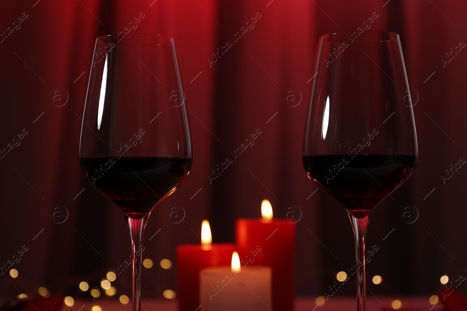 Photo of Burning candles and wine in glasses on table against blurred lights, closeup