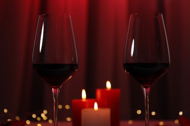 Burning candles and wine in glasses on table against blurred lights, closeup