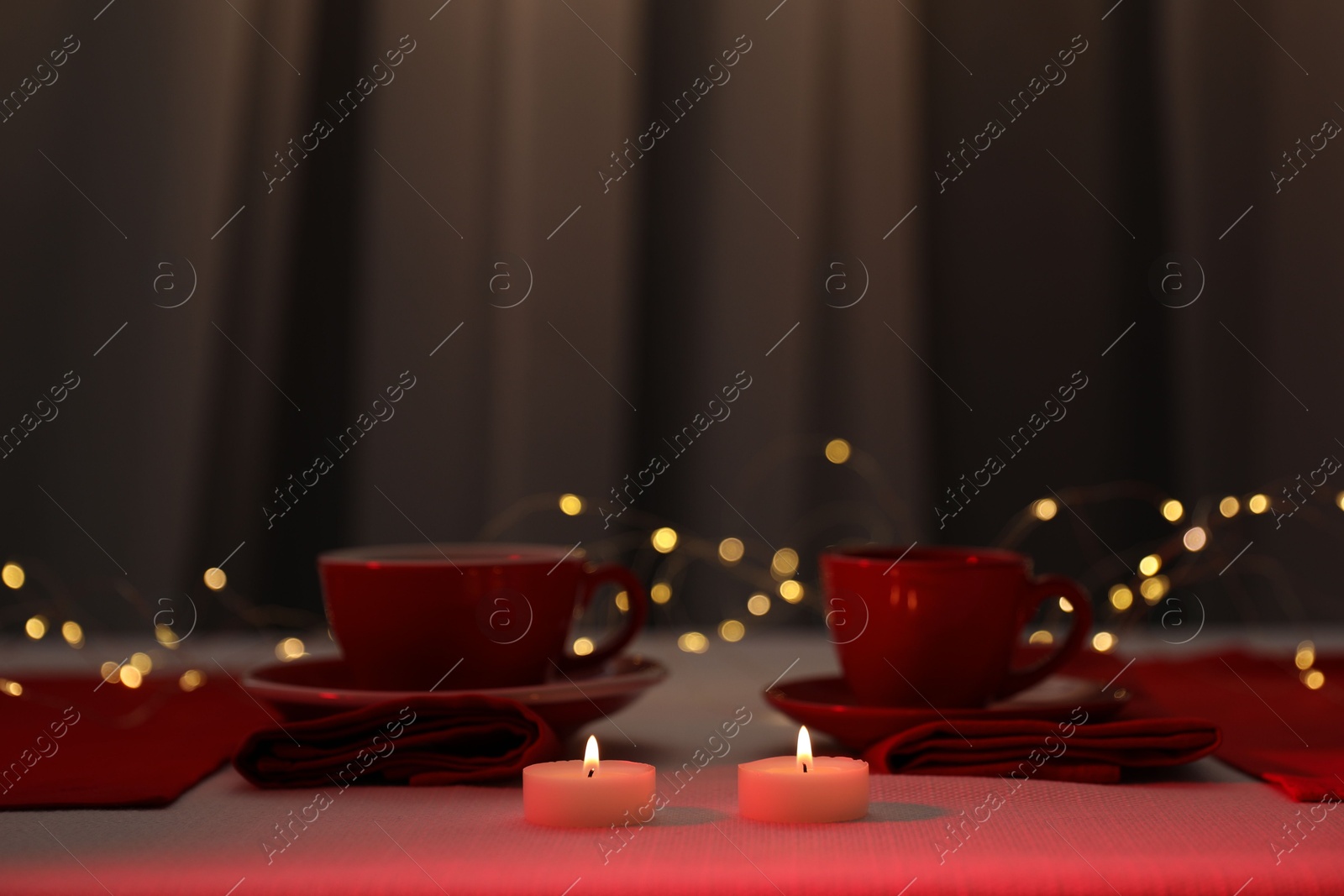 Photo of Burning candles and cups on table against blurred lights