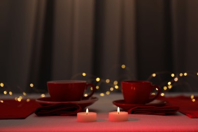 Photo of Burning candles and cups on table against blurred lights