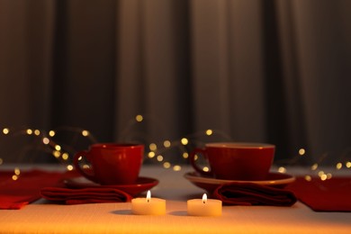 Photo of Burning candles and cups on table against blurred lights