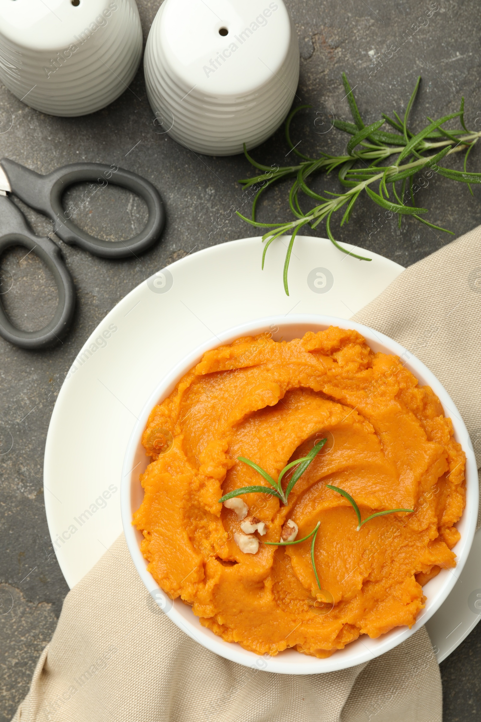 Photo of Delicious mashed sweet potatoes in bowl and spices on gray textured table, flat lay