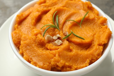 Photo of Delicious mashed sweet potatoes with rosemary and nuts in bowl on table, closeup