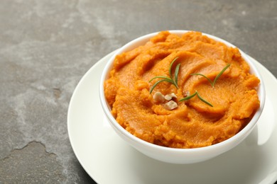 Photo of Delicious mashed sweet potatoes with rosemary and nuts in bowl on gray textured table, closeup