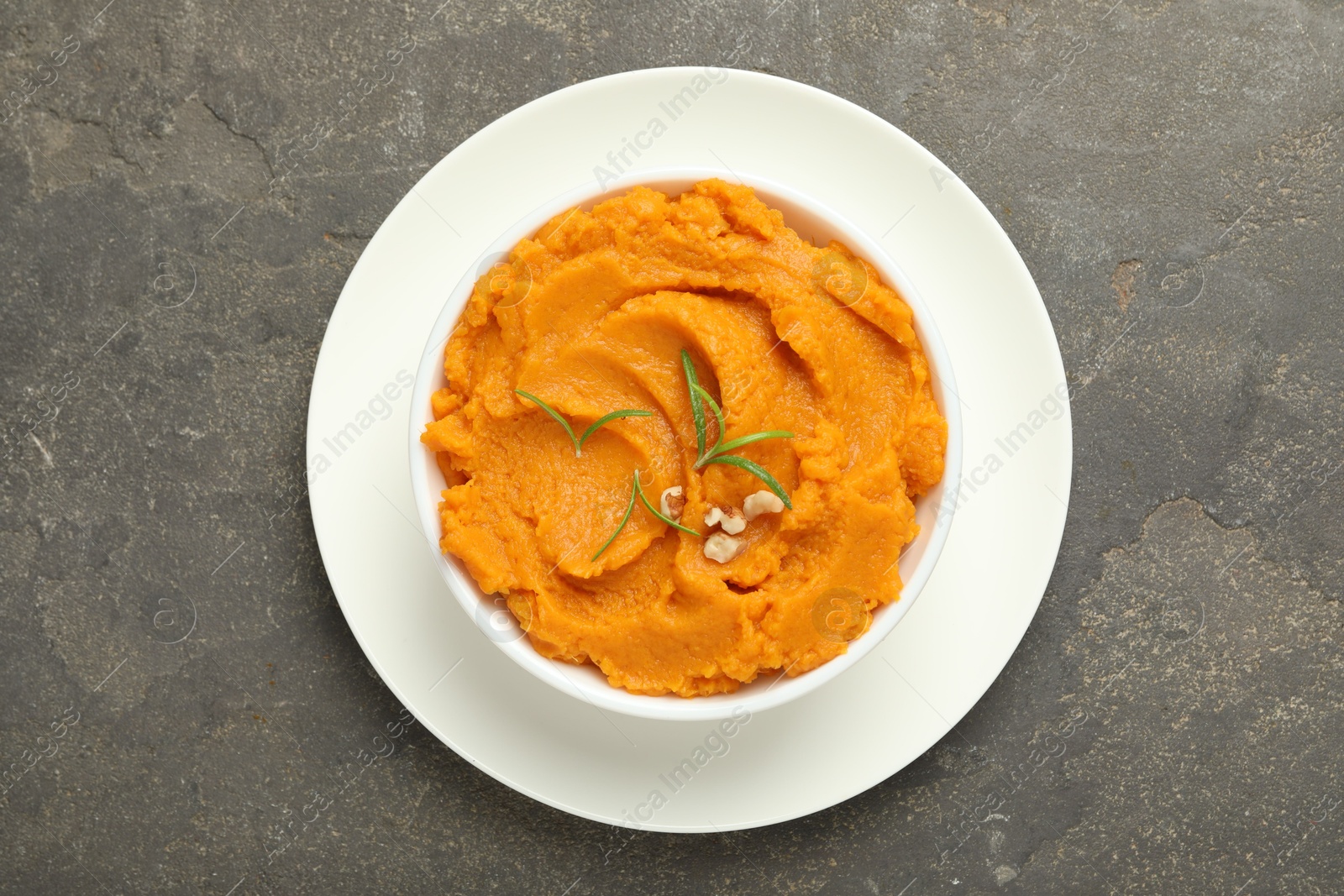 Photo of Delicious mashed sweet potatoes with rosemary and nuts in bowl on gray textured table, top view