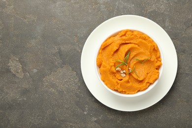 Photo of Delicious mashed sweet potatoes with rosemary and nuts in bowl on gray textured table, top view. Space for text