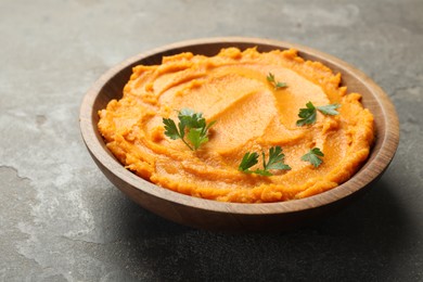 Photo of Delicious mashed sweet potatoes with parsley in bowl on gray textured table, closeup