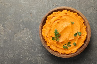 Photo of Delicious mashed sweet potatoes with parsley in bowl on gray textured table, top view. Space for text