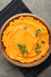 Photo of Delicious mashed sweet potatoes with parsley in bowl on gray textured table, top view