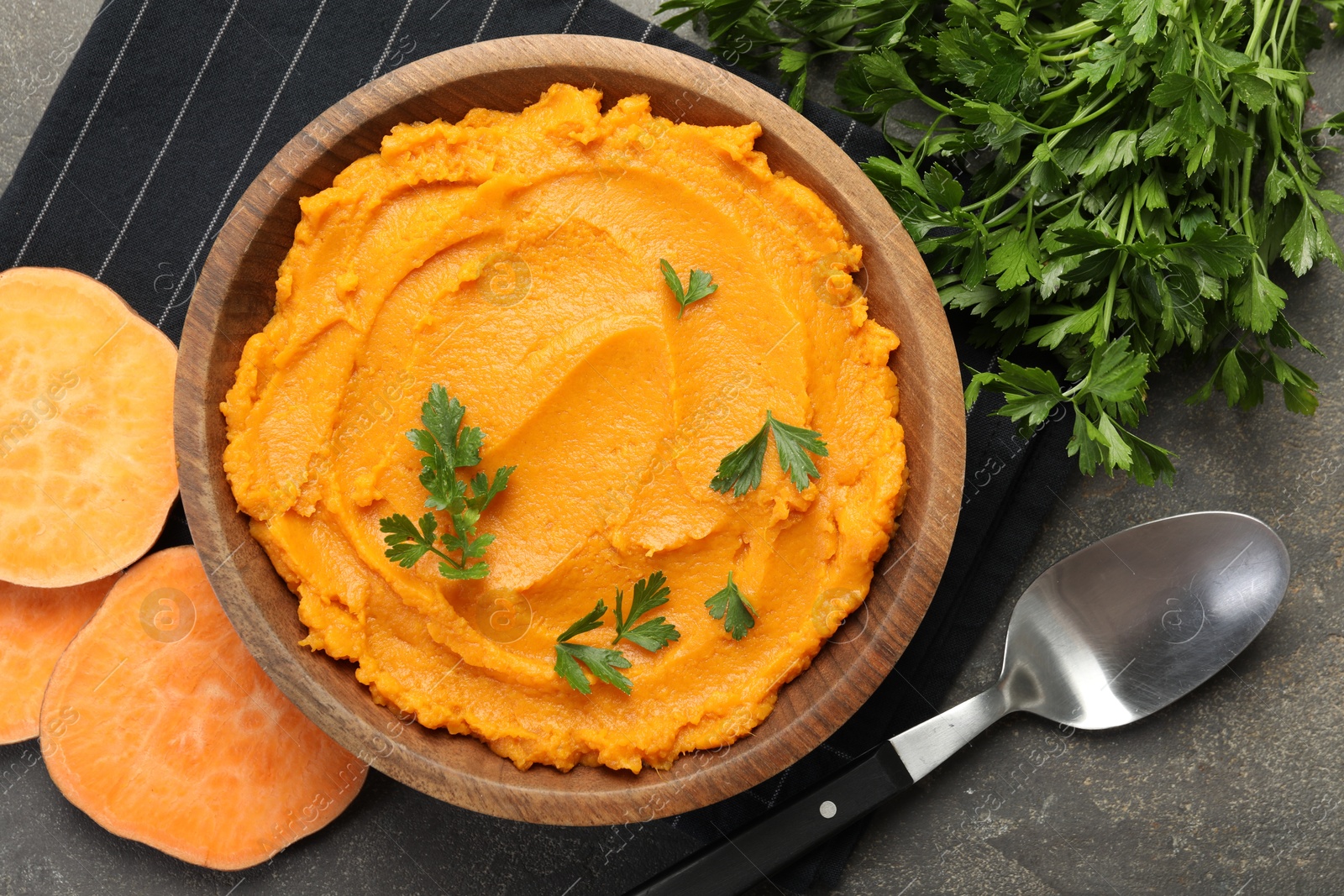 Photo of Delicious mashed sweet potatoes with parsley served on gray textured table, flat lay