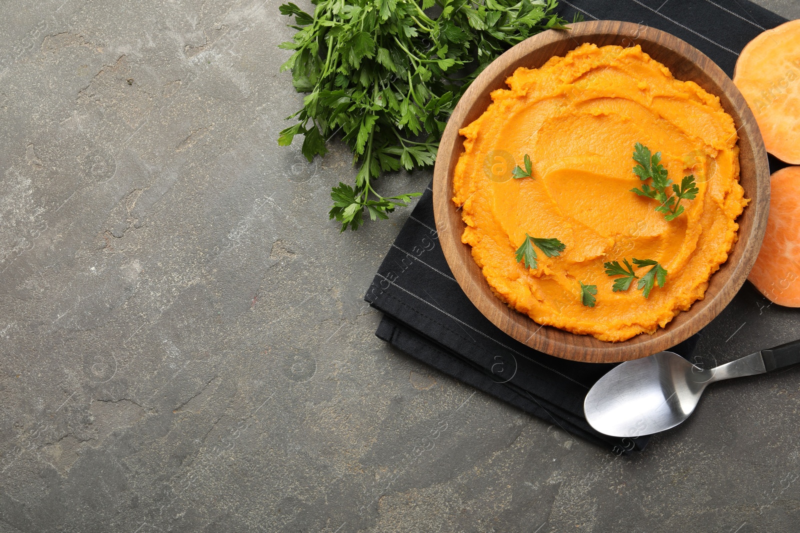 Photo of Delicious mashed sweet potatoes with parsley served on gray textured table, flat lay. Space for text