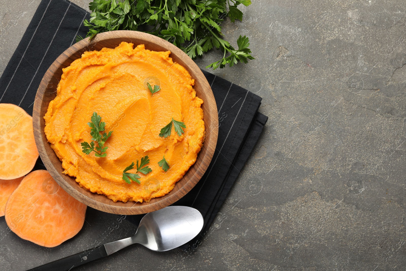 Photo of Delicious mashed sweet potatoes with parsley served on gray textured table, flat lay. Space for text