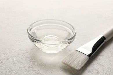 Photo of Peeling procedure. Chemical peel liquid in bowl and brush on white table, closeup