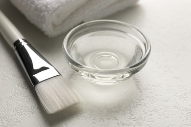 Photo of Peeling procedure. Chemical peel liquid in bowl, towel and brush on white table, closeup