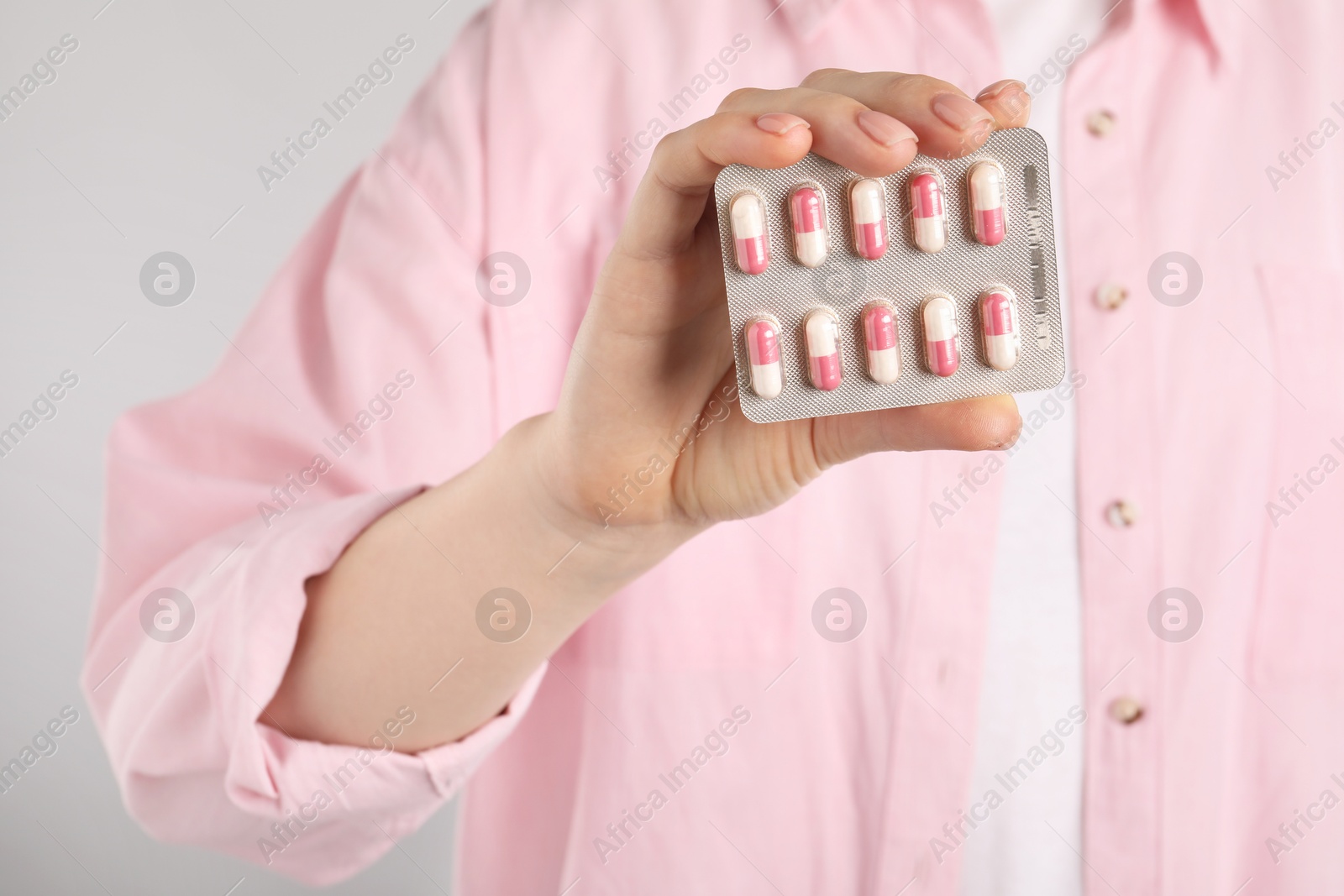 Photo of Woman holding blister with antibiotic pills on light grey background, closeup