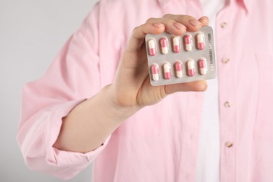 Photo of Woman holding blister with antibiotic pills on light grey background, closeup