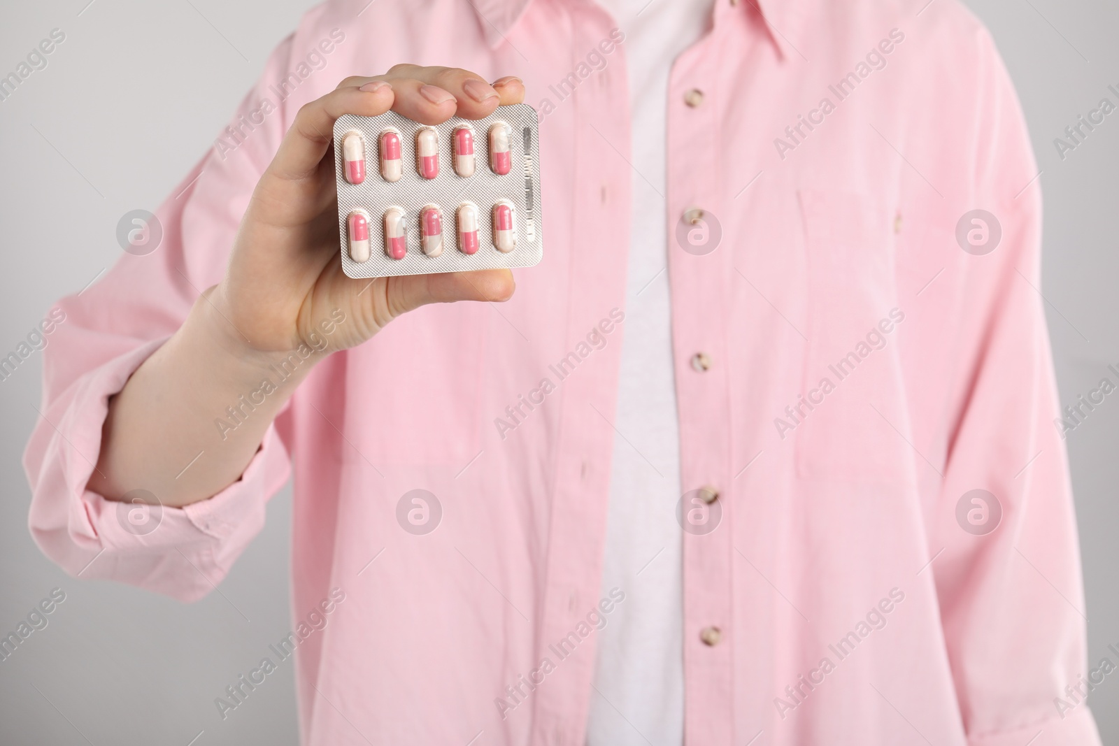 Photo of Woman holding blister with antibiotic pills on light grey background, closeup