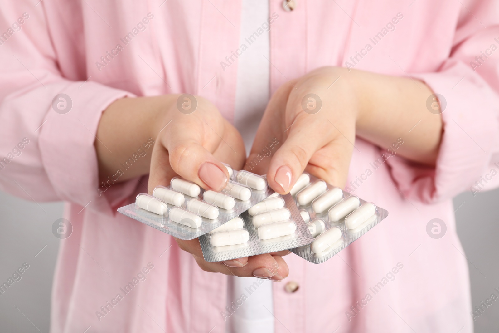 Photo of Woman holding blisters with antibiotic pills on light grey background, closeup