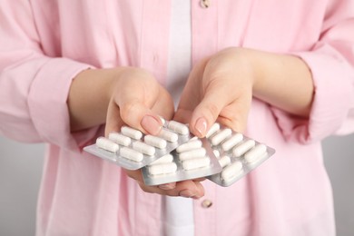 Woman holding blisters with antibiotic pills on light grey background, closeup