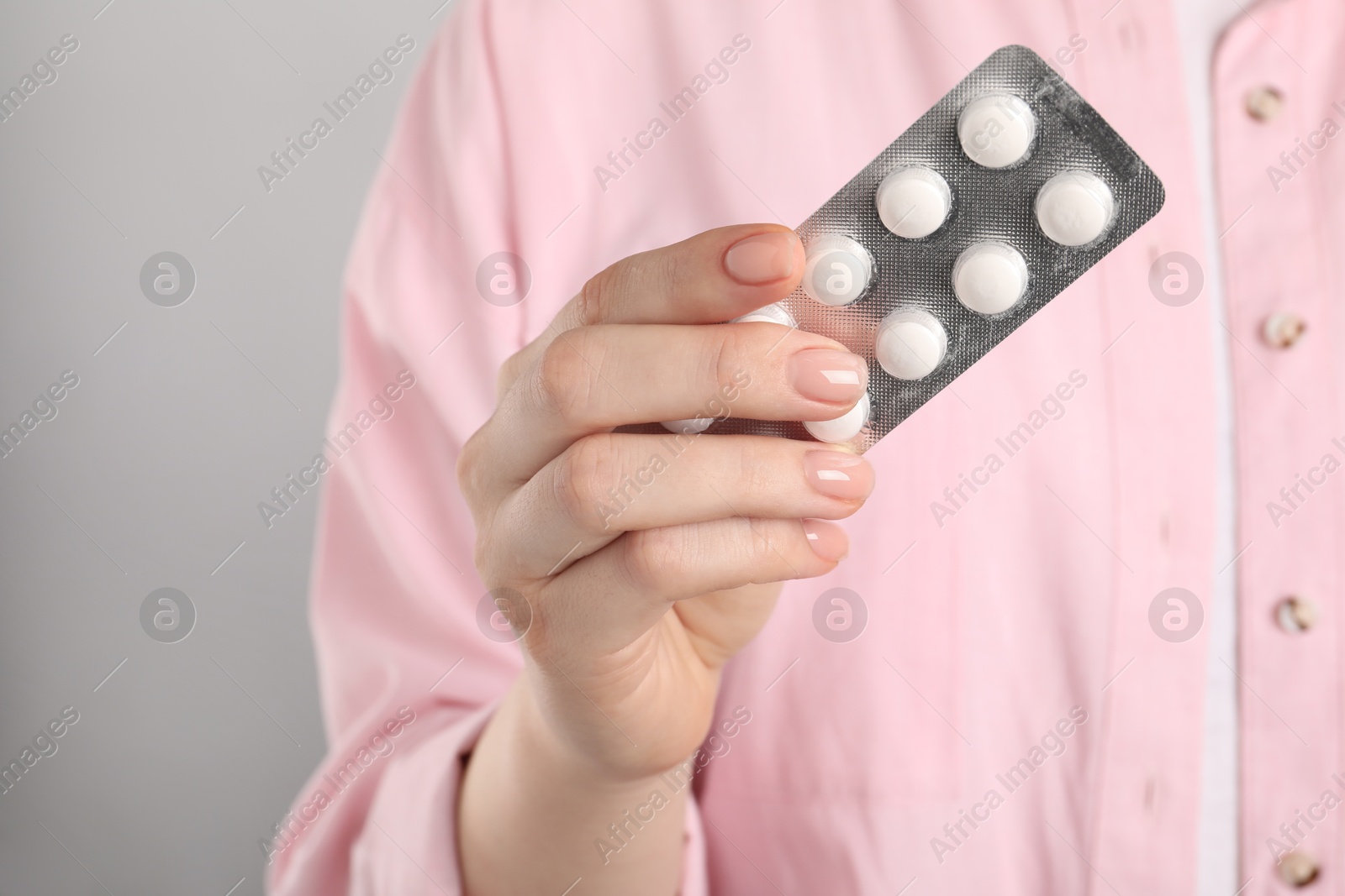 Photo of Woman holding blister with antibiotic pills on light grey background, closeup