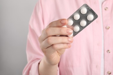 Photo of Woman holding blister with antibiotic pills on light grey background, closeup