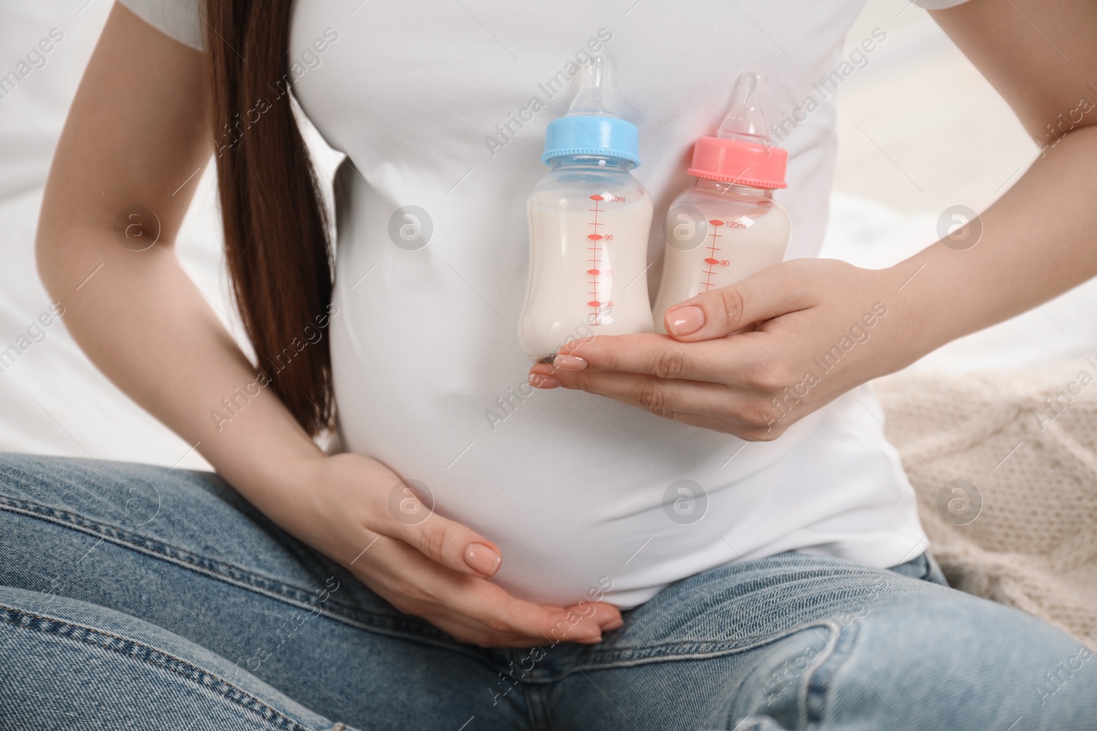 Photo of Expecting twins. Pregnant woman holding two bottles with milk at home, closeup