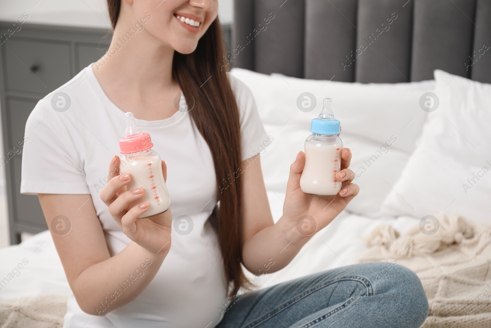 Photo of Expecting twins. Pregnant woman holding two bottles with milk at home, closeup