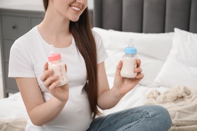 Photo of Expecting twins. Pregnant woman holding two bottles with milk at home, closeup