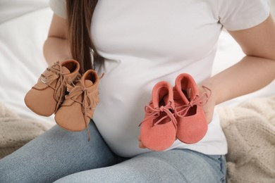 Expecting twins. Pregnant woman holding two pairs of shoes at home, closeup