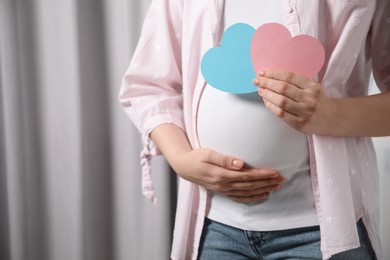 Photo of Expecting twins. Pregnant woman holding two paper cutouts of hearts at home, closeup. Space for text