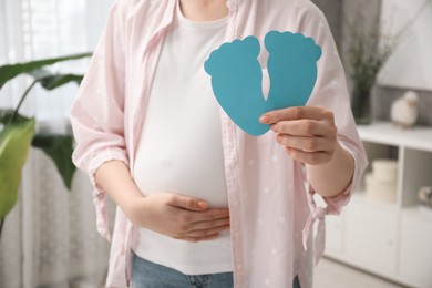 Expecting twins. Pregnant woman holding two paper cutouts of feet at home, closeup