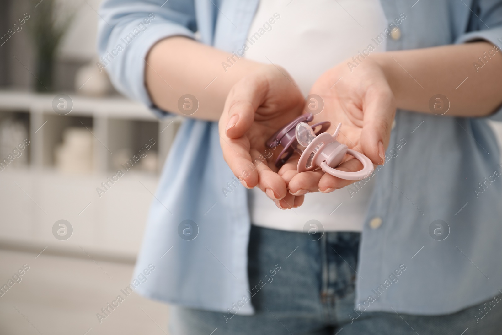 Photo of Expecting twins. Pregnant woman holding two pacifiers at home, closeup