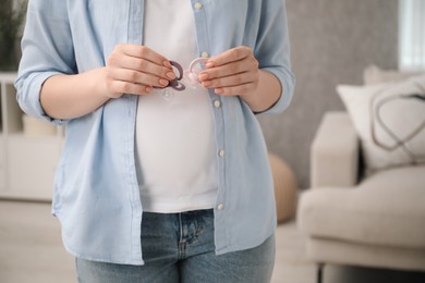 Expecting twins. Pregnant woman holding two pacifiers at home, closeup