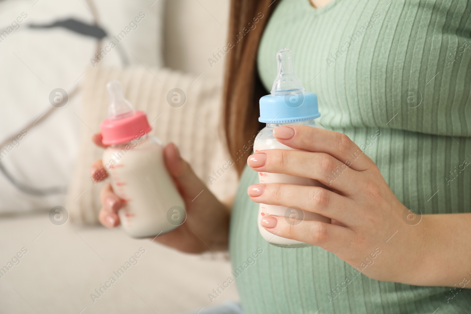 Photo of Expecting twins. Pregnant woman holding two bottles of milk at home, closeup