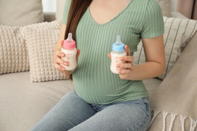 Photo of Expecting twins. Pregnant woman holding two bottles of milk at home, closeup