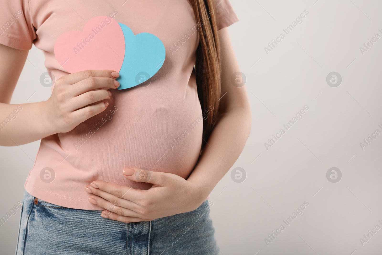 Photo of Expecting twins. Pregnant woman holding two paper cutouts of hearts on light grey background, closeup. Space for text