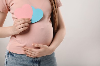 Expecting twins. Pregnant woman holding two paper cutouts of hearts on light grey background, closeup. Space for text