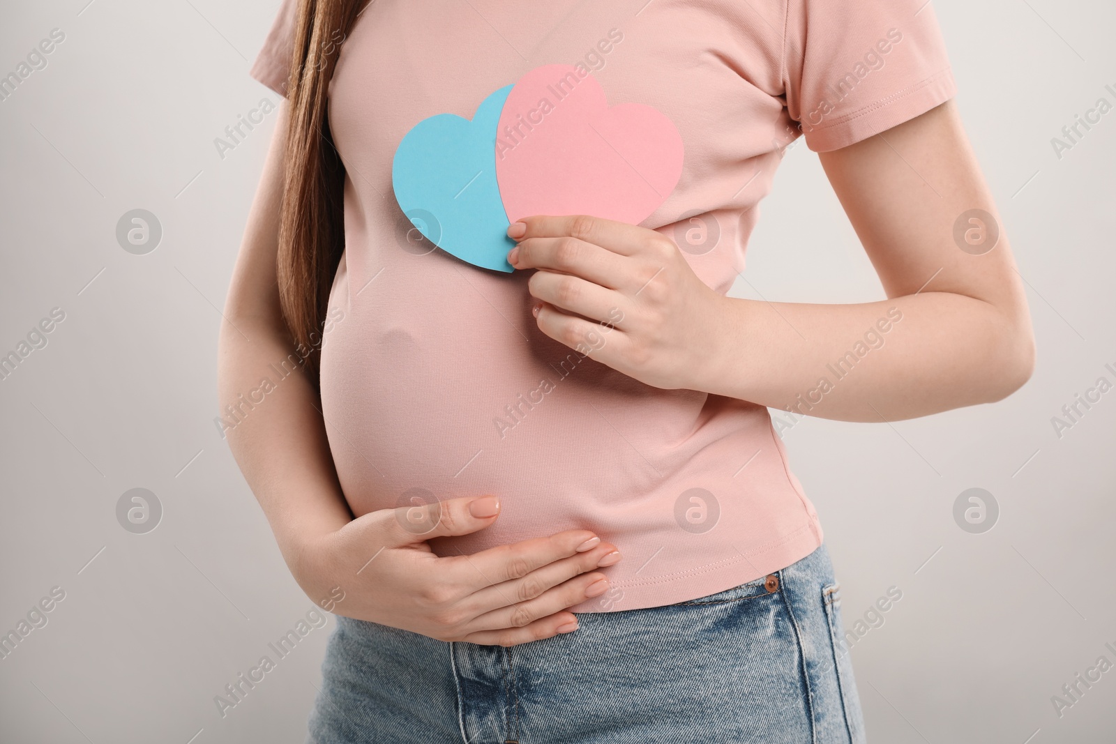 Photo of Expecting twins. Pregnant woman holding two paper cutouts of hearts on light grey background, closeup