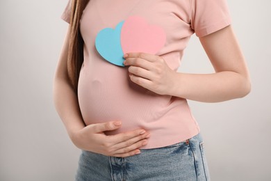 Photo of Expecting twins. Pregnant woman holding two paper cutouts of hearts on light grey background, closeup