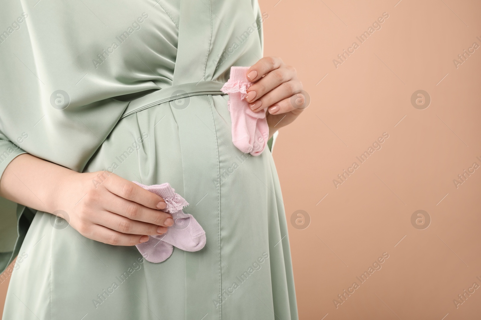 Photo of Expecting twins. Pregnant woman holding two pairs of socks on light brown background, closeup. Space for text