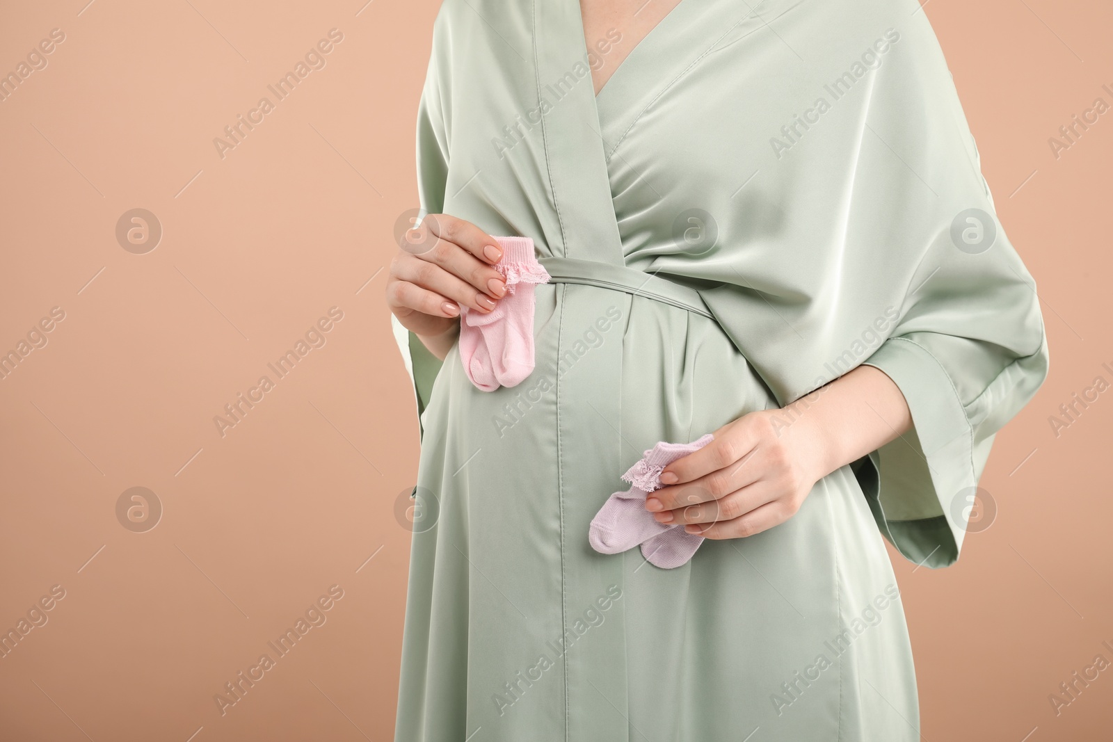 Photo of Expecting twins. Pregnant woman holding two pairs of socks on light brown background, closeup. Space for text